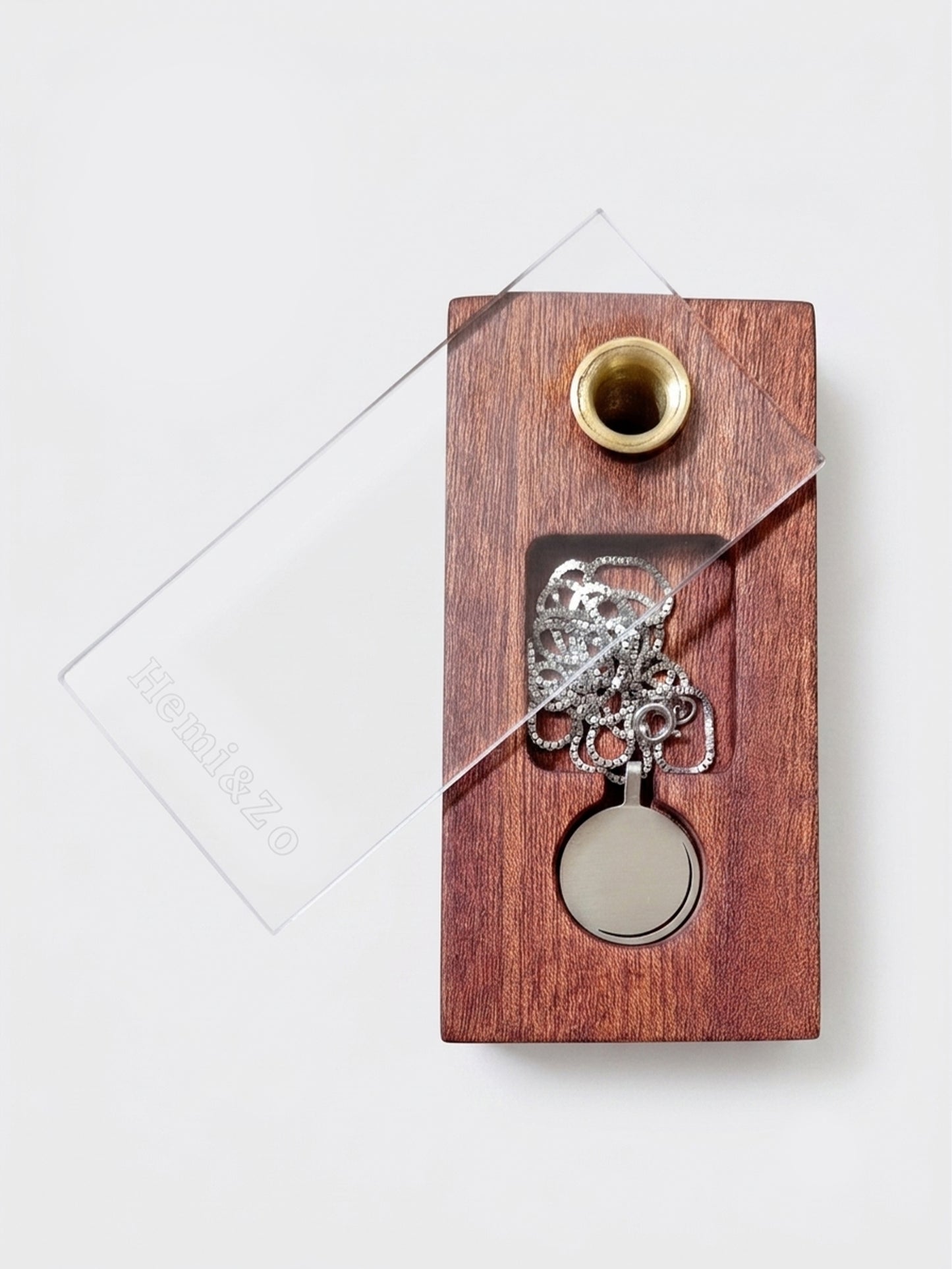 A rectangular wooden jewelry box with a rich brown grain, containing a white gold chain and a moon phase pendant, set against a clean, light gray background. The transparent acrylic lid is slid open to the side, featuring the engraved logo "Hemi&Zo".