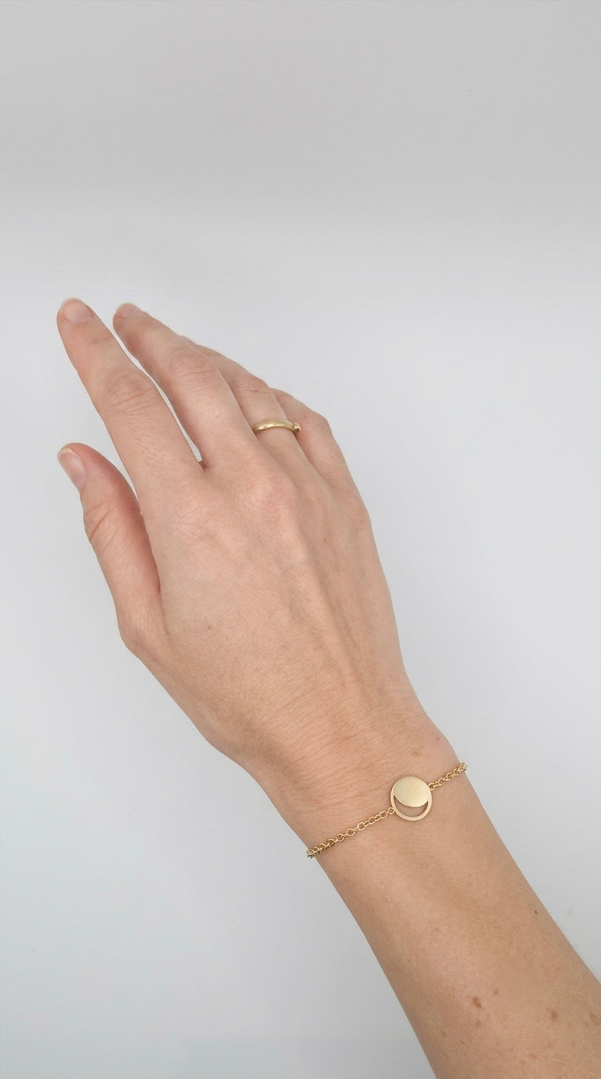Hand wearing a gold moon phase bracelet on a plain background