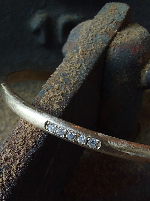 Detail view of Hemi & Zo gold bangle with four diamonds, set against a backdrop of studio tools