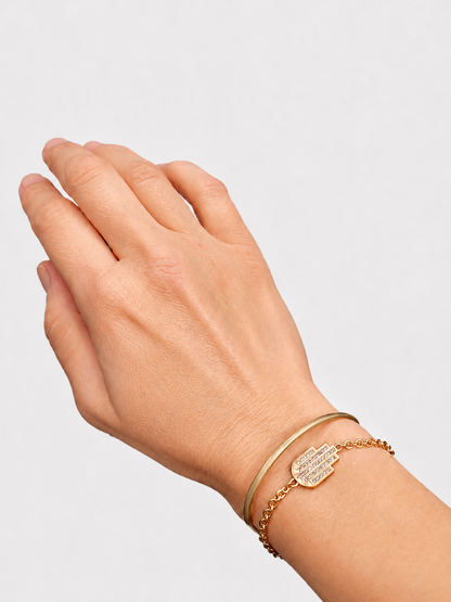Hand wearing a gold hamsa bracelet on a light gray background