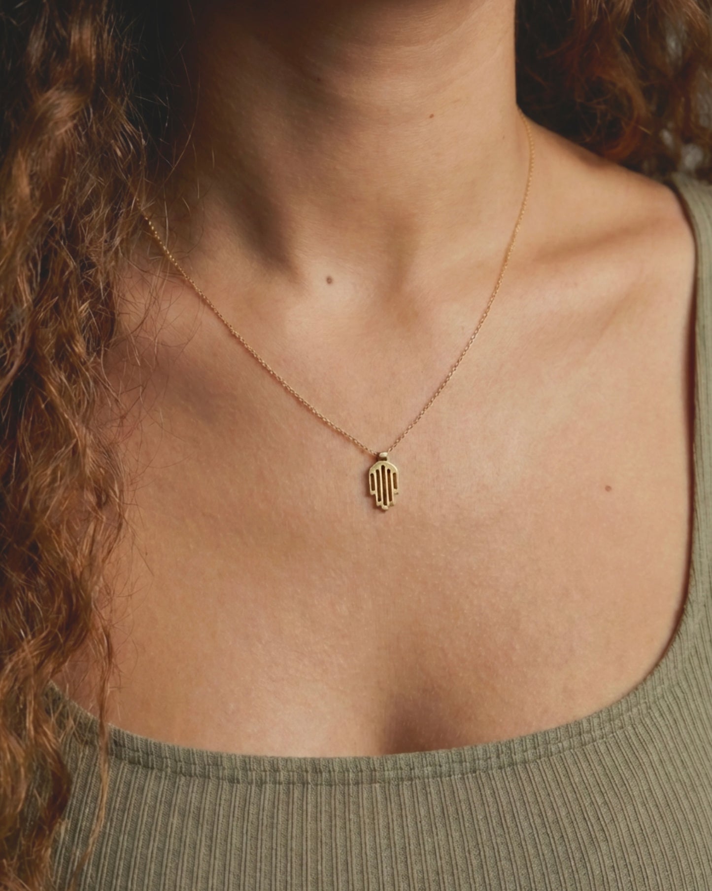 Hemi and Zo Gold necklace with a pendant on a person wearing a green top.