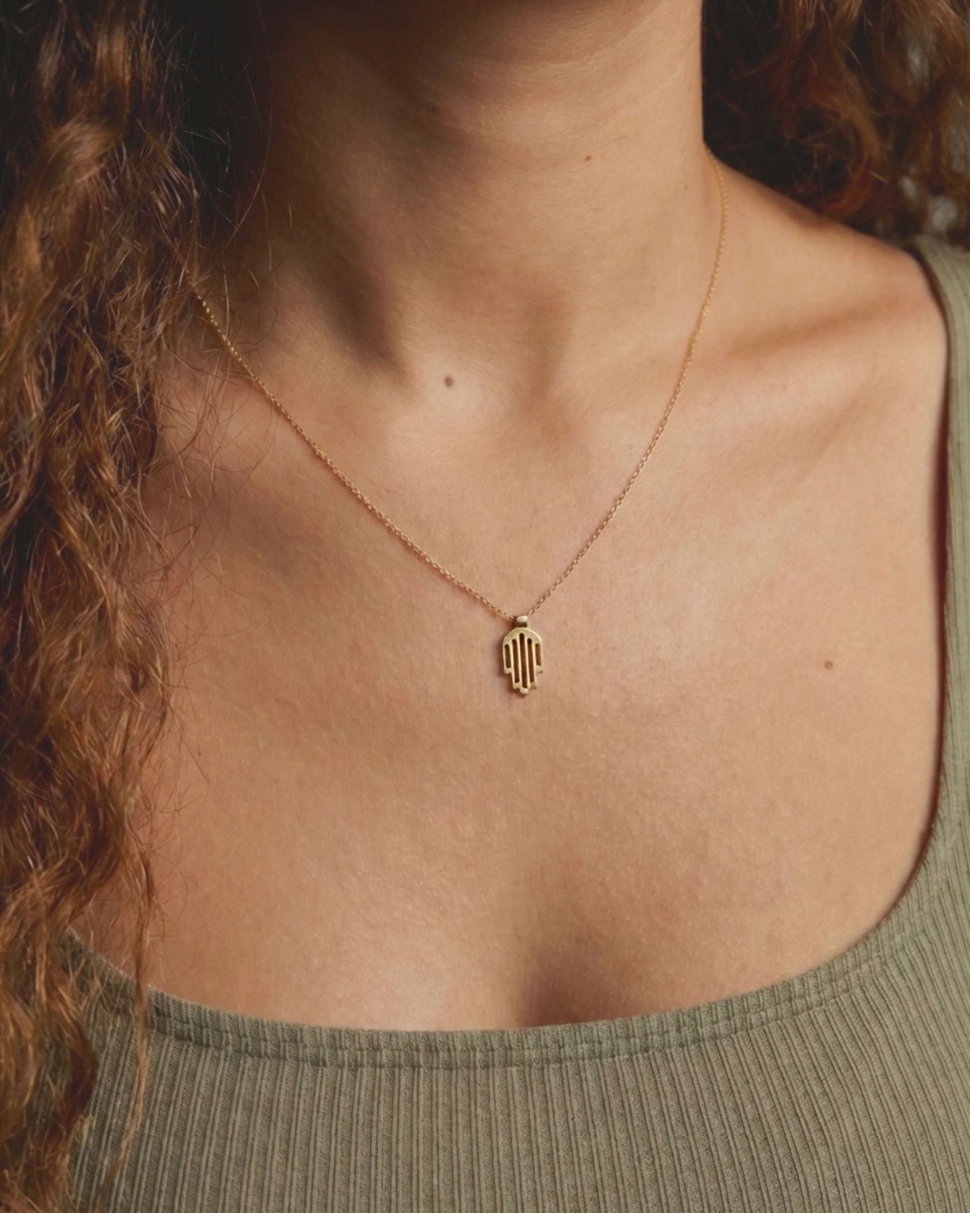 Hemi and Zo Gold necklace with a pendant on a person wearing a green top.