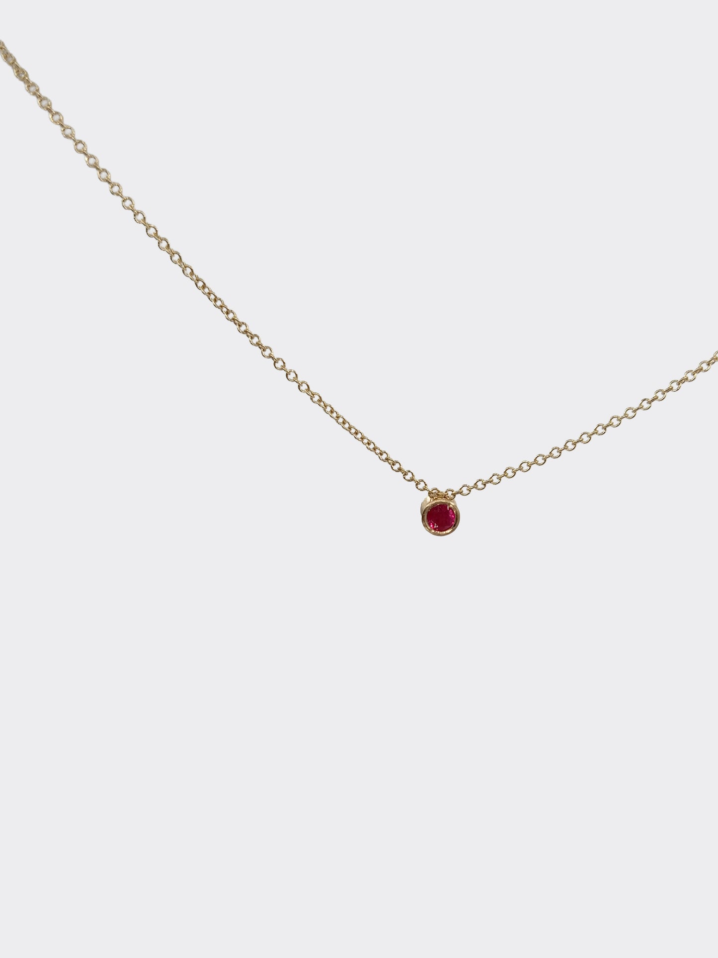 Gold necklace with a red gemstone pendant on a white background