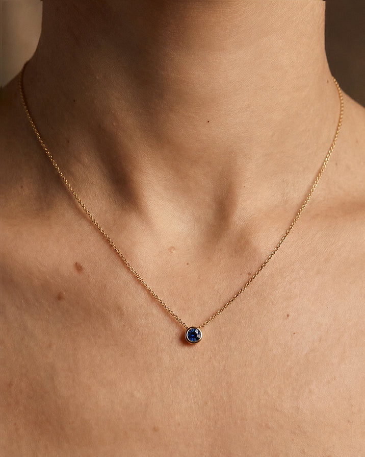 Gold necklace with a blue gemstone on a person's neck