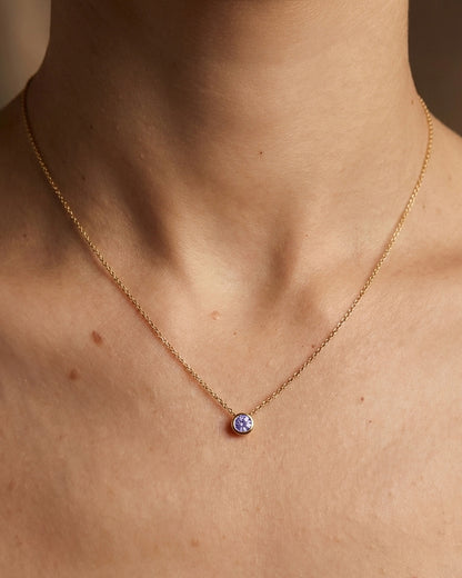 Gold necklace with a small round purple pendant on a person's neck