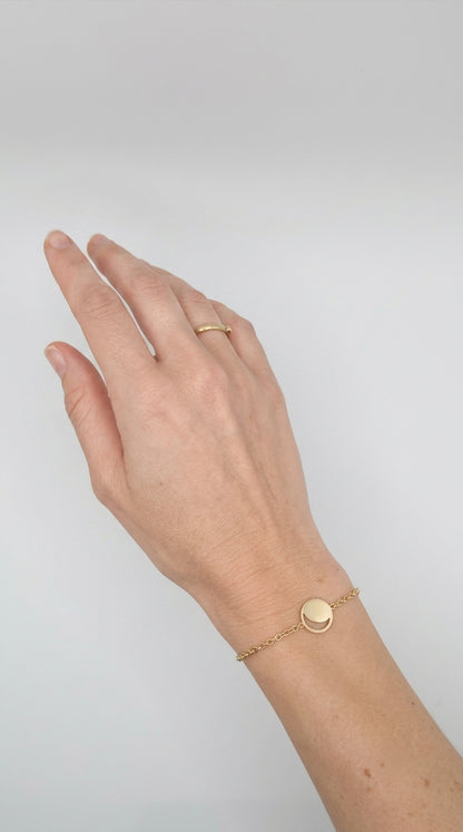 Hand wearing a gold moon phase bracelet on a plain background