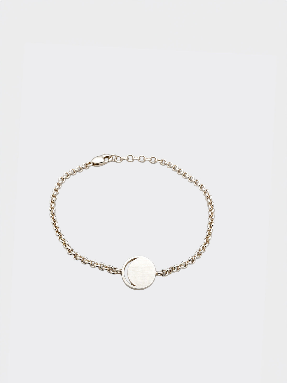 Hemi & Zo delicate silver chain bracelet with a flat, circular disc moon phase charm in the center, displayed on a clean, light gray background.