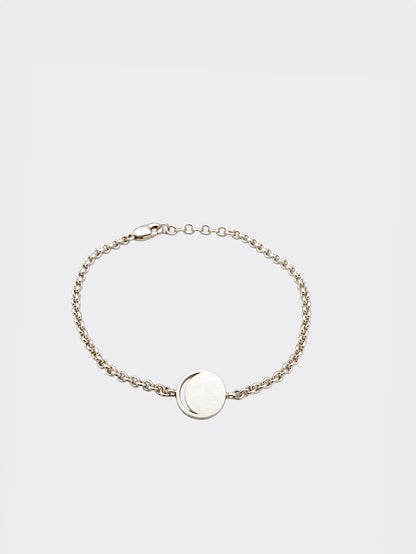 Hemi & Zo delicate silver chain bracelet with a flat, circular disc moon phase charm in the center, displayed on a clean, light gray background.