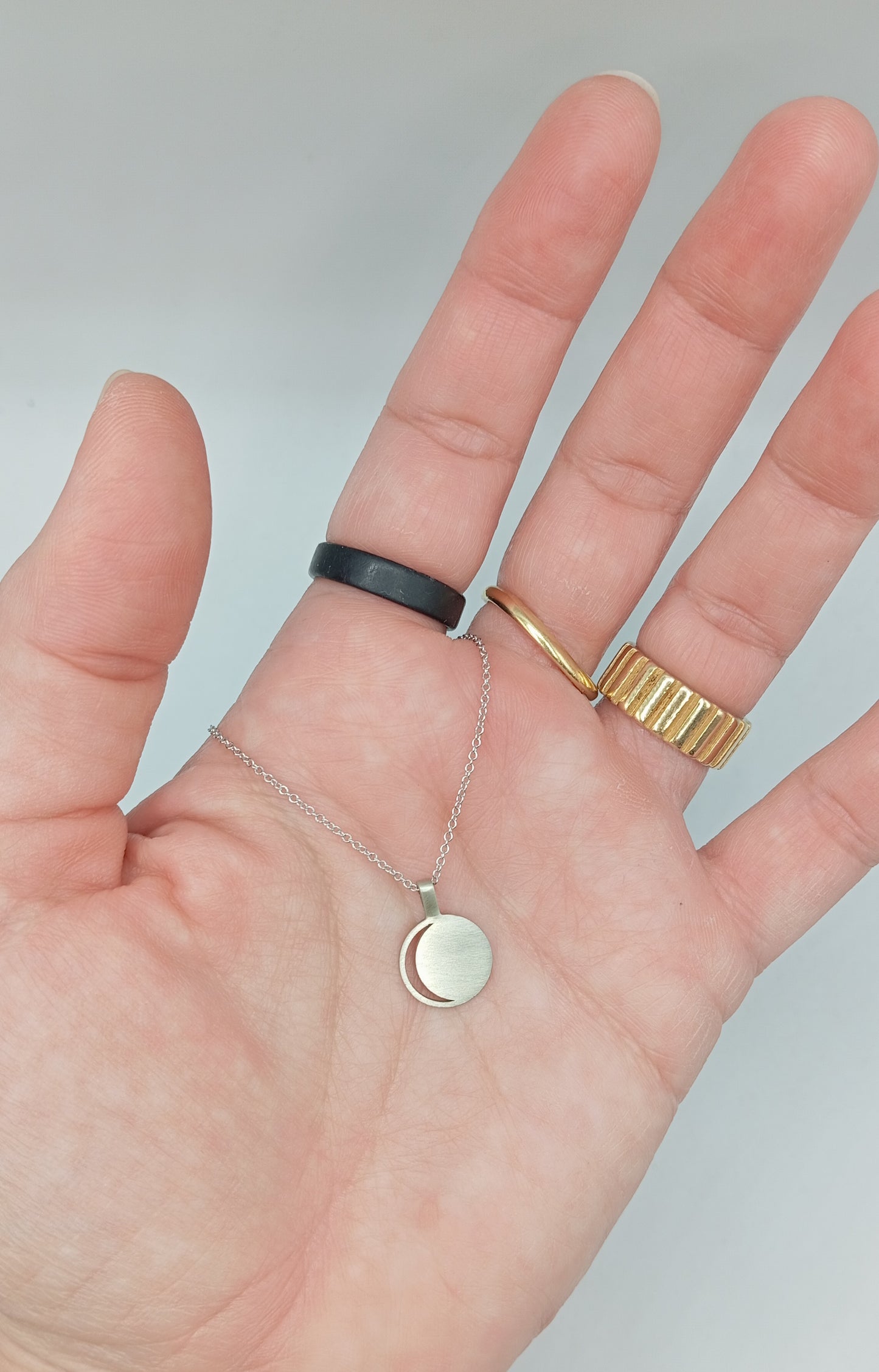 Hand wearing a gold ring and  white gold necklace with a moon design on a plain background