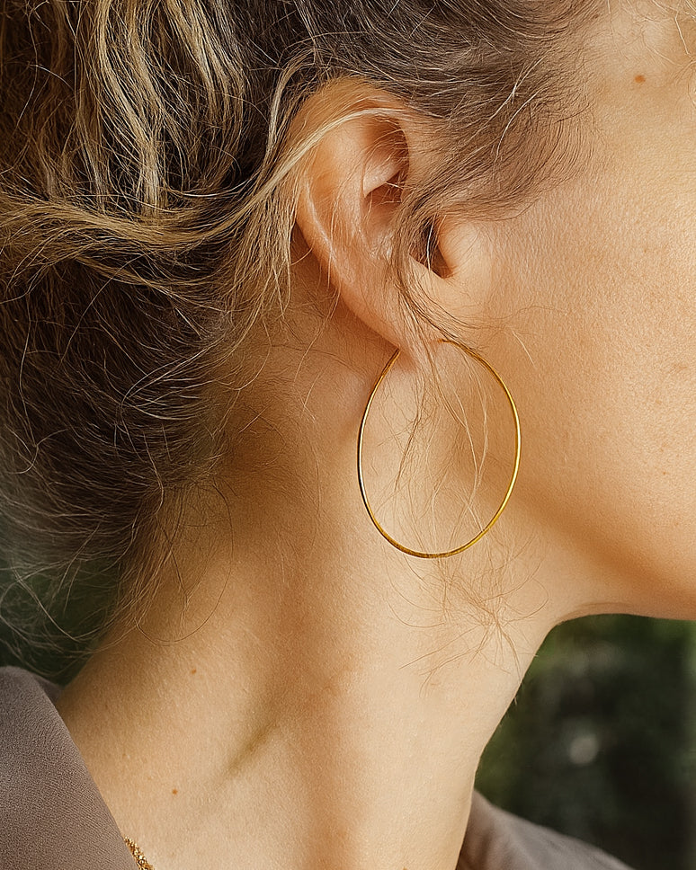 Gold teardrop hoop earrings on a womn's ear